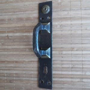 May include: A vintage door handle with a black metal handle and a brass plate. The handle has a simple design and is attached to a rectangular plate with a keyhole.