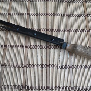 May include: A black metal hand saw with a wooden handle. The saw has a small metal loop at the end of the handle.