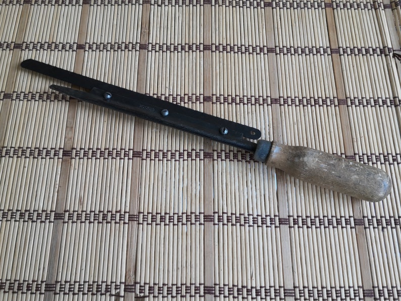 May include: A black metal hand saw with a wooden handle. The saw has a small metal loop at the end of the handle.