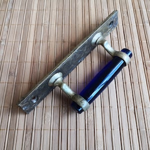 Puede incluir: Una manija de puerta vintage con un inserto de vidrio azul. La manija es de latón y tiene una base rectangular.