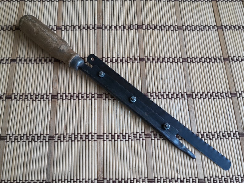 May include: A long, thin, black metal tool with a wooden handle. The tool has four screws along the metal blade and a pointed tip.