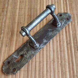 May include: A vintage metal door handle with a keyhole and a long, curved lever. The handle is rusty and has a worn, aged appearance.