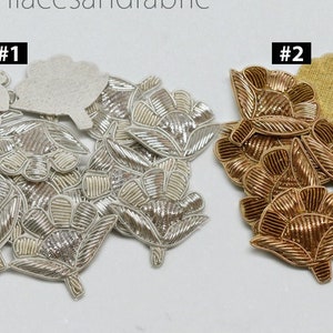 Puede incluir: Dos juegos de aplicaciones de flores bordadas en oro y plata. Las aplicaciones tienen la forma de una flor con un centro y pétalos. Las aplicaciones están sobre un fondo blanco. #1 y #2 están escritos encima de cada juego de aplicaciones.