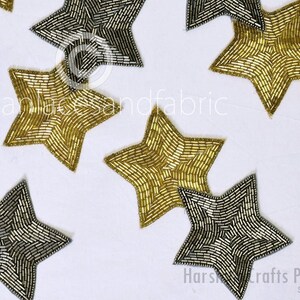 Può includere: Dieci decorazioni a forma di stella dorate e argentate con un design a perline. Le stelle sono disposte in modo casuale su uno sfondo bianco.