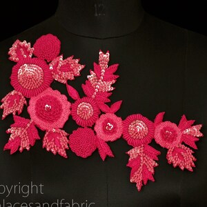 May include: Pink floral applique with sequins and beads. This embellishment features a cluster of flowers with leaves and is perfect for adding a touch of elegance to clothing or crafts.