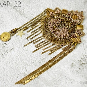 May include: A gold-toned embroidered patch with a star and coin charm. The patch has a circular design with a fringe of gold chains.
