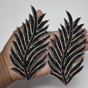 Pode incluir: Dois enfeites de folhas pretas com contas e detalhes de fio dourado. Os enfeites medem aproximadamente 15 cm de comprimento e 7,5 cm de largura.