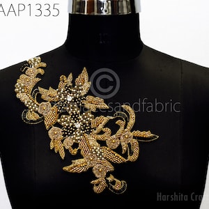 May include: Gold and black beaded applique with a floral design. The applique is on a black mannequin.