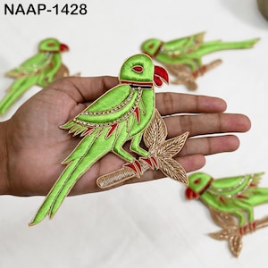 May include: Embroidered parrot patches in shades of green, red, and gold. The patches feature intricate details, including beaded accents and a perched design. The text "NAAP-1428" is visible in the upper left corner.