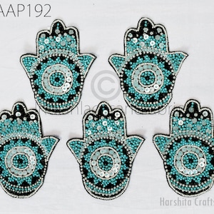 以下が含まれることがあります： 邪悪な目をデザインしたターコイズブルーとシルバービーズのハmsaハンドチャーム5個。ハmsaハンドは、保護と幸運の象徴として人気があります。