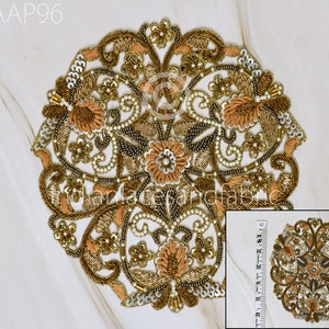 May include: A circular gold and peach embroidered applique with a floral design. The applique is approximately 4 inches in diameter.