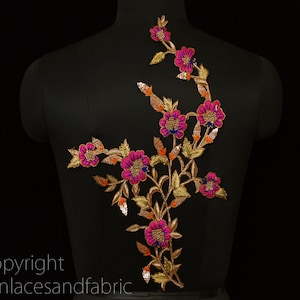 Op de afbeelding: Een bloemenapplicatie met roze en blauwe bloemen, gouden bladeren en oranje accenten. De applicatie is op een zwarte achtergrond.