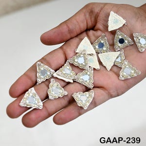 May include: A collection of 14 white triangular fabric patches with silver trim and a small mirror in the center. The patches are arranged in a hand, with the text "GAAP-239" visible at the bottom of the image.