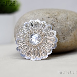 May include: A silver and gold embroidered flower applique with a clear rhinestone center. The applique is on a white background.