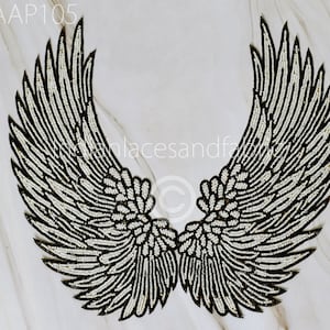 May include: A pair of black and white beaded angel wings. The wings are made of small white beads sewn onto a black fabric base.