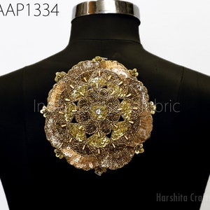 May include: A gold and beige circular applique with sequins and beads. The applique is on a black mannequin.