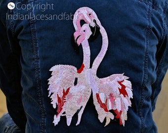 Könnte beinhalten: Eine Jeansjacke mit einem pinkfarbenen und roten Pailletten-Flamingo-Applikationen auf der Rückseite.