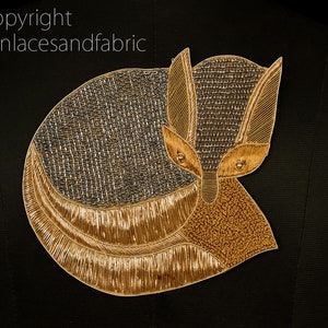 May include: A gold and silver embroidered fox applique. The fox is curled up with its tail wrapped around its body. The applique is perfect for adding a touch of whimsy to any project.