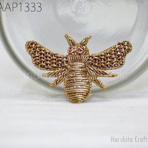 May include: A gold embroidered bee with red eyes. The bee is a decorative patch or applique.