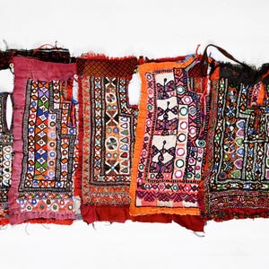 Può includere: Cinque pannelli di tessuto ricamato colorati con intricati motivi geometrici e decorazioni a specchio. I pannelli sono realizzati in tessuto rosso, arancione, nero, bianco e blu.