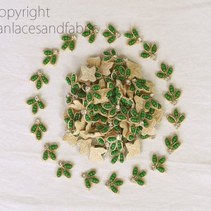 Puede incluir: Una colección de adornos en forma de hoja verde y dorada con un strass en el centro. Los adornos están dispuestos en un círculo alrededor de una pila de adornos similares.
