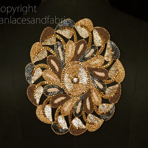 May include: A circular gold, brown, and silver beaded applique with a floral design. The applique is perfect for adding a touch of elegance to clothing or crafts.