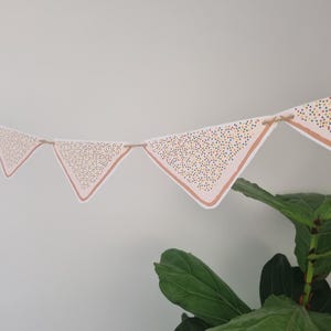 May include: A pink and white bunting with a sprinkle pattern. The bunting is strung with twine and has a triangular shape.