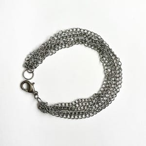 May include: A silver-coloured multi-strand chain bracelet with a lobster clasp closure. The bracelet features multiple fine chains, creating a layered effect. The background is plain white.