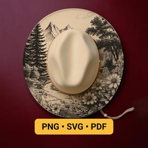 May include: Cream-colored hat with a landscape design. The hat features a beige crown and a wide brim decorated with a black and white mountain and forest scene. The text "PNG • SVG • PDF" is displayed on a yellow rectangle.
