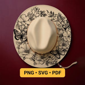 May include: A cream-colored fedora hat with a wide brim, adorned with a black floral and butterfly design. The hat features a tan band and a chin strap. The image includes the text "PNG • SVG • PDF" on a yellow background.