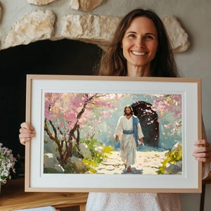 May include: A framed painting depicting a man in white robes walking through a garden with blooming pink trees. The man is walking towards a stone archway with a dark opening. The painting is in a light wood frame.