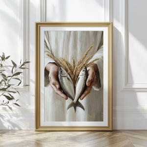 May include: A framed print featuring a painting of two fish and wheat stalks held in cupped hands. The artwork is set against a white background and framed in gold. The painting has a religious theme.