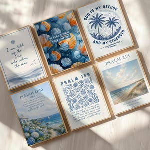 May include: A collection of framed art prints with coastal and religious themes. The prints feature ocean scenes, seashells, and inspirational quotes. Colors include blue, white, and beige. The frames are a light wood color. The prints are arranged on a light wood surface.