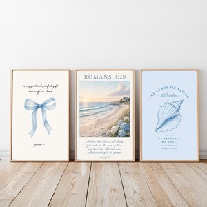 Könnte beinhalten: Drei gerahmte Kunstdrucke mit inspirierenden Zitaten. Die Drucke zeigen eine Aquarellschleife, eine Strandszene mit dem Text "Römer 8:28" und eine Muschel mit dem Text "Er führt mich an stillen Wassern". Die Rahmen sind hellbraun.