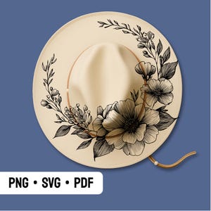 May include: A cream-colored wide-brim hat featuring a black line-art floral illustration that wraps around the crown. The design includes detailed petals, leaves, and stems. A thin brown cord with a small bead accent is attached to the hat brim.