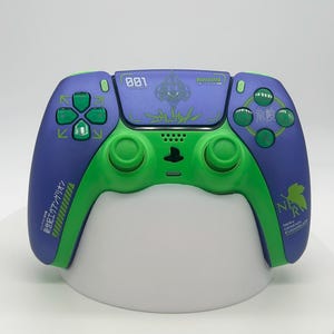 May include: A purple and green video game controller featuring the text 001, NERV, and Japanese characters. The controller includes a directional pad, two analog sticks, and action buttons with green accents on a purple and green body.