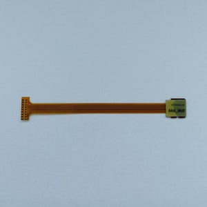 May include: A gold-coloured flexible circuit board with a connector on one end and a small rectangular chip on the other end. The chip has the text "MICROCHIP" and "AAA_MOD" printed on it.