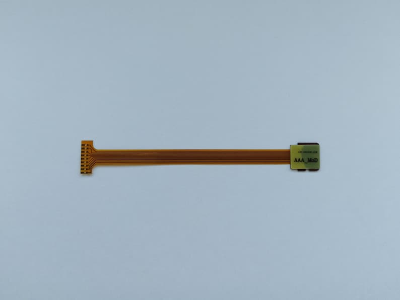 May include: A gold-coloured flexible circuit board with a connector on one end and a small rectangular chip on the other end. The chip has the text "MICROCHIP" and "AAA_MOD" printed on it.