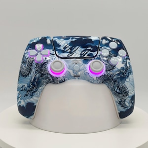 May include: A wireless video game controller featuring a blue and white dragon and wave pattern across the shell. The device includes white analogue sticks, a directional pad, and action buttons, with bright pink LED lighting around the sticks.