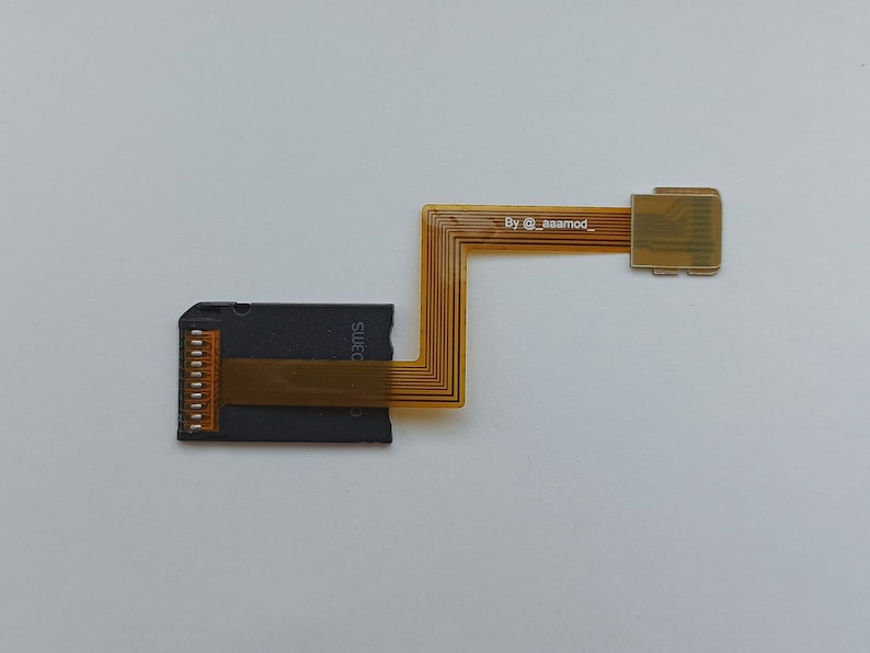May include: A black and gold circuit board with a gold ribbon cable connector. The ribbon cable is labelled "By @aaamod_"