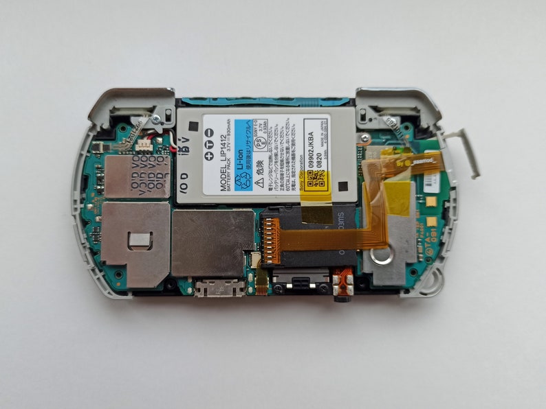 May include: A disassembled white handheld gaming console with a green circuit board, a gold ribbon cable, and a battery pack labelled "MODEL LIP1412 Li-ion Battery Pack 3.7V".