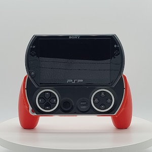 Könnte beinhalten: Schwarze Sony PSP-Handheld-Spielkonsole mit rotem Griff. Die Konsole verfügt über einen schwarzen Bildschirm, Steuertasten und das PSP-Logo. Der rote Griff bietet einen komfortablen Halt.