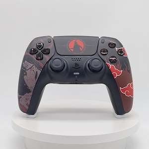 Puede incluir: Un mando de videojuegos inalámbrico negro con gráficos personalizados. El lado izquierdo muestra una ilustración de un personaje, mientras que el derecho presenta patrones de nubes rojas. Un emblema circular rojo está centrado en el panel táctil.