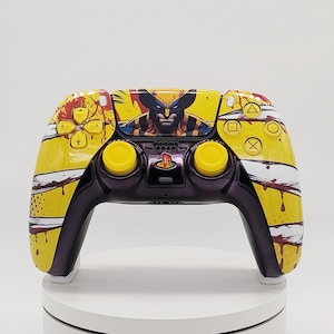 Puede incluir: Un mando de videojuegos inalámbrico con un diseño en amarillo y morado, que presenta una ilustración gráfica del personaje Wolverine en el panel táctil central. El mando incluye joysticks amarillos y detalles de marcas de garras blancas.
