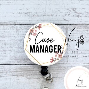 May include: A white and gold badge reel with a floral design and the text "Case Manager". The badge reel is attached to a black retractable cord and a clear plastic badge holder. The badge reel also features a small pink and gold circle with the text "Vanj Reels & Handmade Goods".