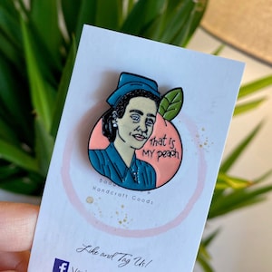 May include: A blue and pink enamel pin featuring a cartoon woman with a blue hat and the text "That is my peach". The pin is on a white background with the text "Boo Handcraft Goods" and "Like and Tag Us! Vanj Hand Made Designs -Ohmybadge".