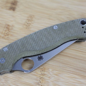 May include: A green and silver pocket knife with a textured handle and a spider logo on the blade.