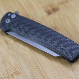 May include: A black folding knife with a carbon fibre handle and a silver blade.