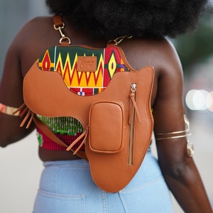 Puede incluir: Un bolso de cuero marrón cruzado con una solapa estampada de colores y un pequeño bolsillo con cremallera. El bolso tiene la forma del continente africano.