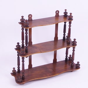 Può includere: Un ripiano in legno a tre livelli con fusi decorativi e una finitura marrone scuro. Il ripiano è progettato per essere montato a parete.